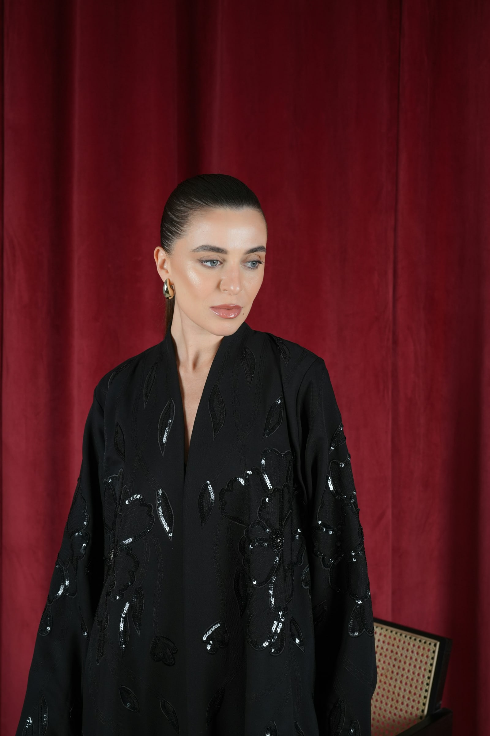 Flowing black occasion abaya against rich burgundy curtains